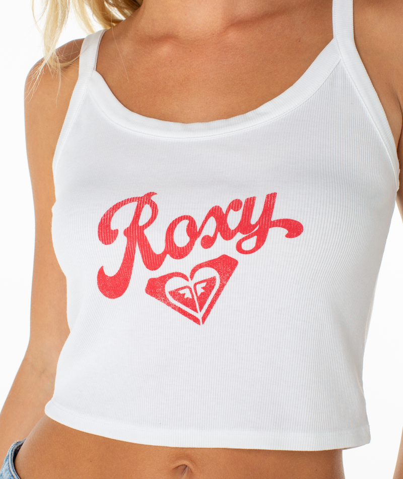 A woman wears the Roxy Home Team Wanderer Tank, a white ribbed cropped top featuring "Roxy" and a red heart logo on the chest—a must-have wardrobe staple.