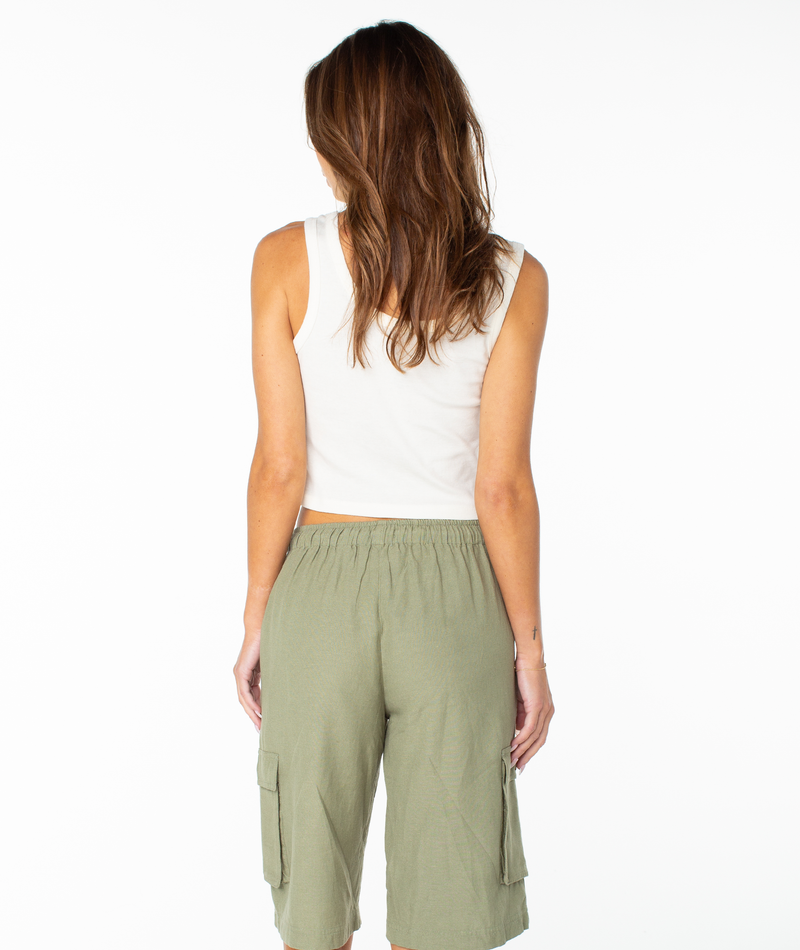 A woman with long brown hair, wearing the Roxy Oceanview Scoop Baby Rib Tank and olive green cargo shorts, stands facing away from the camera against a white background.