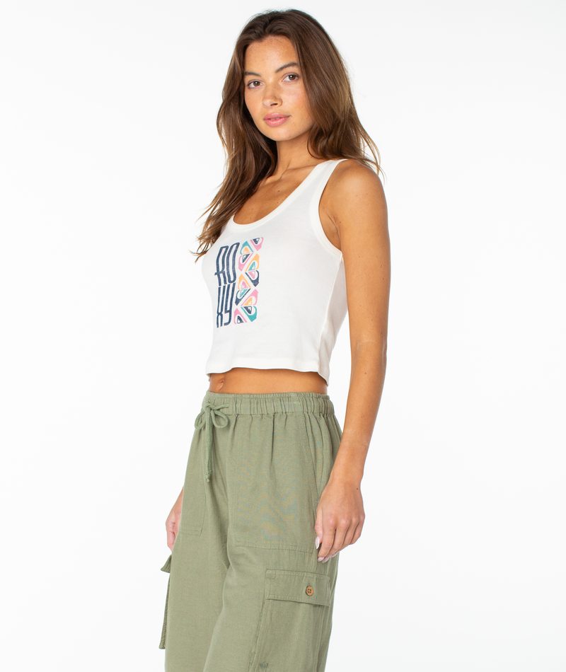 A woman with long brown hair wears the Roxy Oceanview Scoop Baby Rib Tank, inspired by 90s baby tee style, with a colorful geometric design and light green drawstring cargo pants, standing against a plain white background.