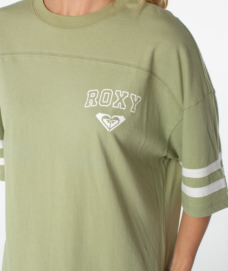 A person is seen wearing a ROXY Game Day Tee in light green, featuring white sleeve stripes and a small logo beneath the text. This boxy-fit top from Roxy showcases retro-inspired details, with only the upper body visible.
