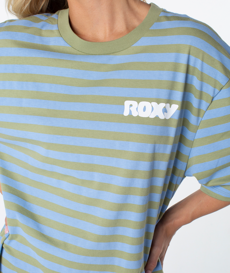 A person is wearing the Roxy Old School Tee, a loose-fitting, short-sleeve T-shirt featuring green and light blue stripes and “ROXY” printed in white across the chest. With its oversized silhouette and relaxed fit, this tee is an essential warm-weather staple. One hand is placed on the hip.