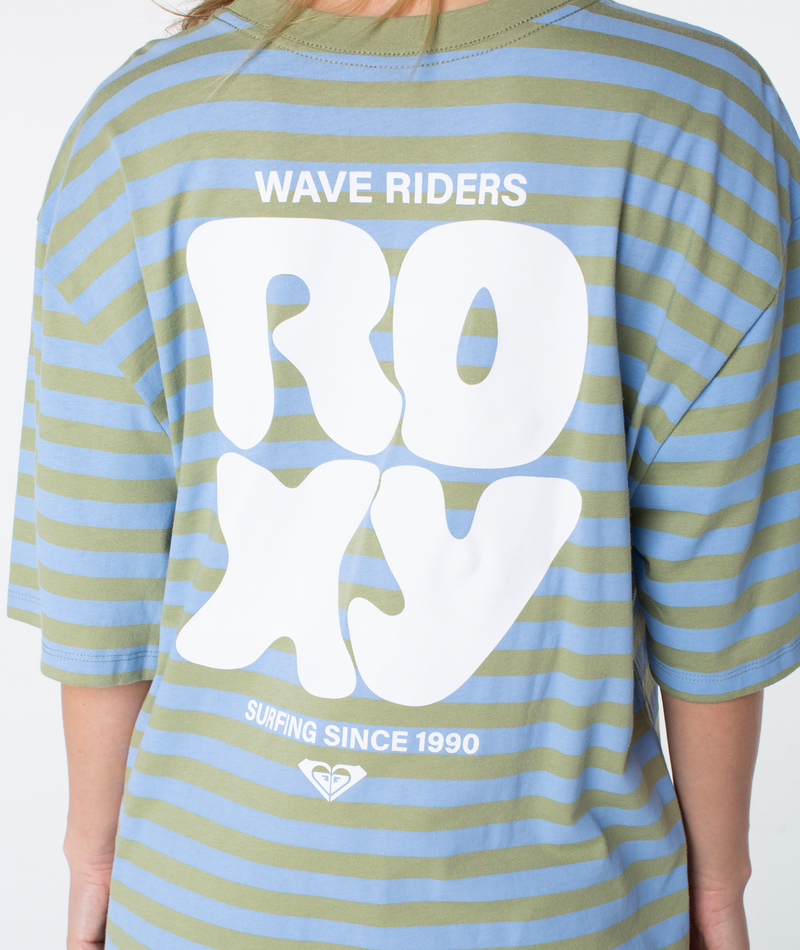 Clad in the Roxy Old School Tee, featuring a blue and green striped design, bold white “WAVE RIDERS ROXY SURFING SINCE 1990” text across the back, and a small heart logo beneath. Its oversized fit makes this tee an essential for relaxed beach days and warm-weather style.
