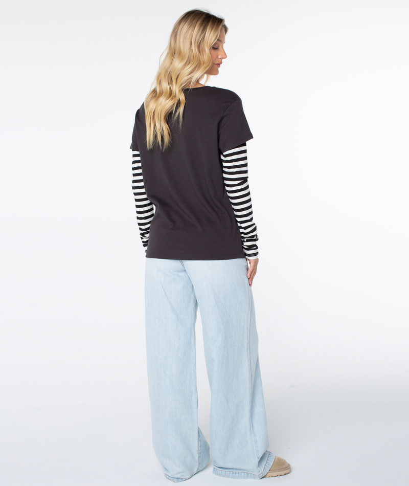 A woman faces away, wearing the Roxy Kinda Salty Two-fer Top, wide-leg light blue jeans, and beige shoes against a white background.