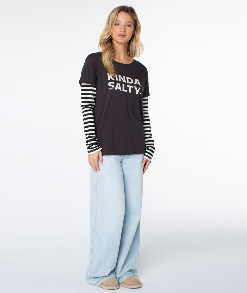A woman faces forward in the Roxy Kinda Salty Two-fer Top in Phantom Kinda Salty, styled with light blue wide-leg jeans and beige shoes against a plain white background for a modern coastal look.