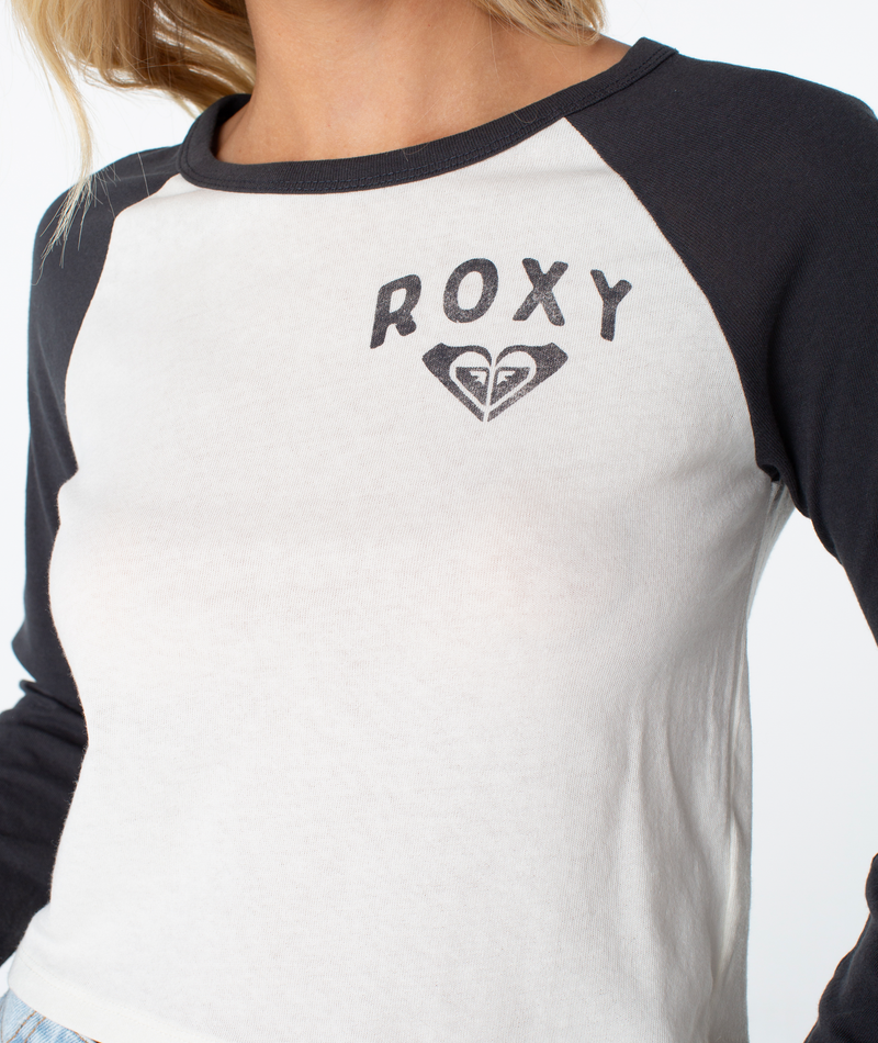 A person is wearing the Roxy Sun Surfboard Boyfriend Raglan Long Sleeve in a black and white colorway, featuring the Roxy logo on the chest. Only their upper body is visible.