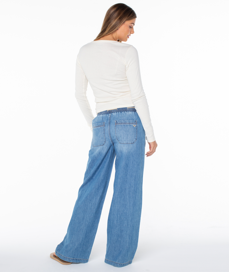 A person seen from behind, wearing a cream-colored Roxy On Holiday Baby Rib Long Sleeve Top and wide-leg blue jeans.