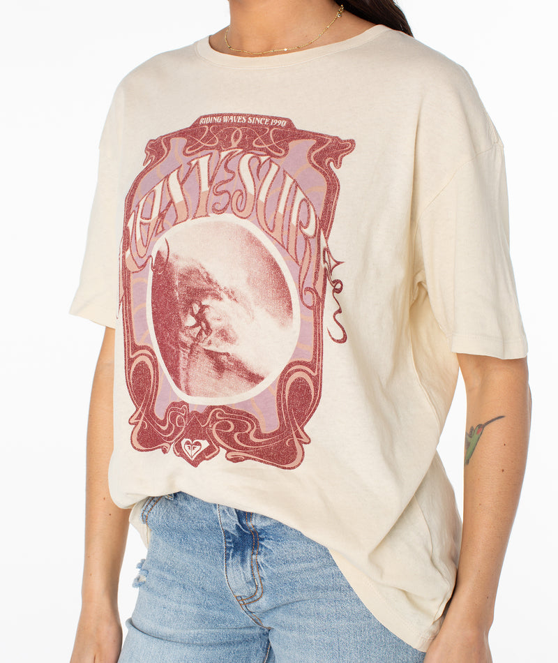 The Barrel Tee is an off-white crewneck t-shirt featuring a vintage-style graphic of a breaking wave inside an ornate border with the text Riding Waves Since 1990.