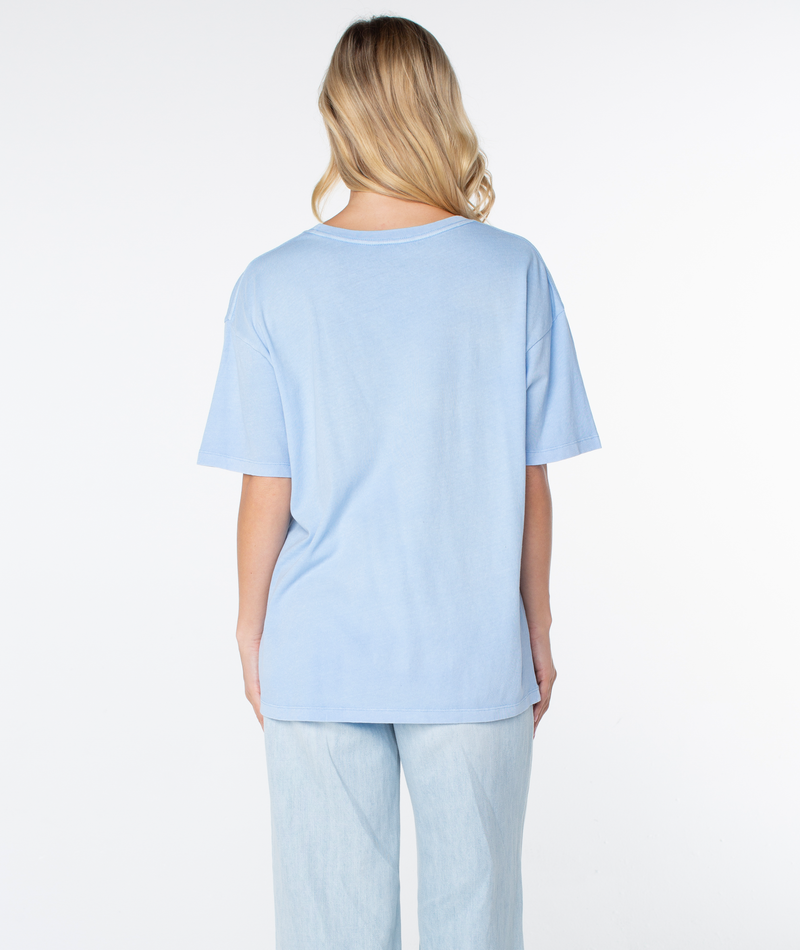 Back view of a person wearing a light blue Roxy On Holiday Top with short sleeves and light-wash jeans.