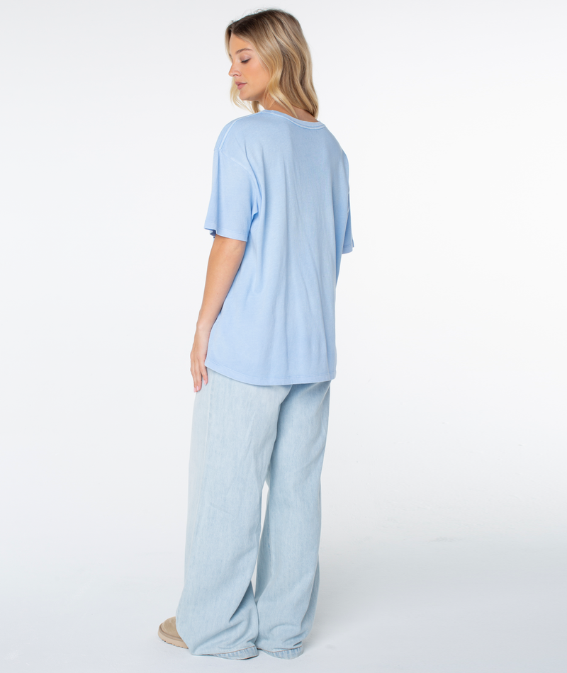 A person seen from behind wearing an oversized light blue Roxy On Holiday Top and wide-leg light-wash jeans.