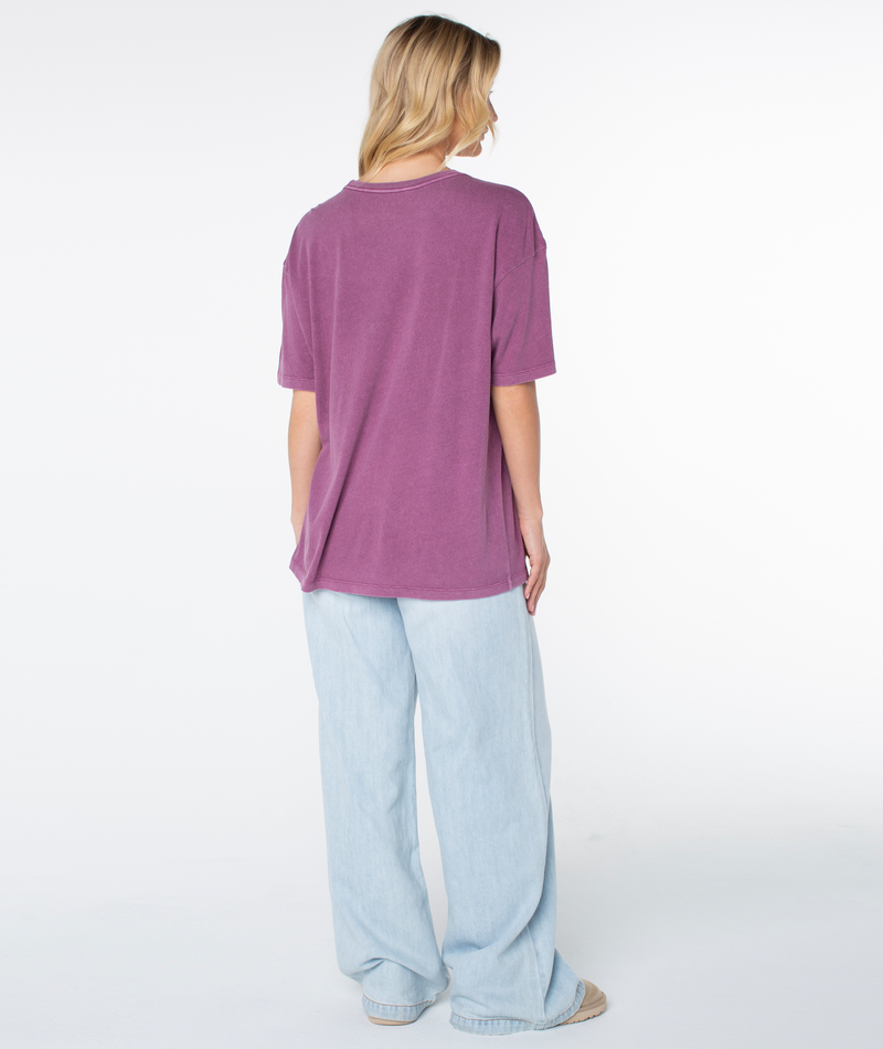 A person seen from the back wearing an oversized, short-sleeved purple Roxy In The Waves Top and loose-fitting light-wash jeans.