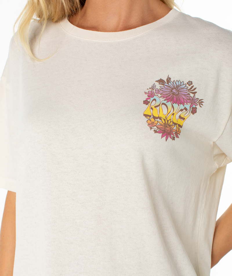 Someone is wearing the Roxy Tribal Sunset Tee, featuring a colorful floral design and "ROXY" on the left chest. The oversized fit with relaxed drop shoulders adds to its casual style. The person's face is not visible.