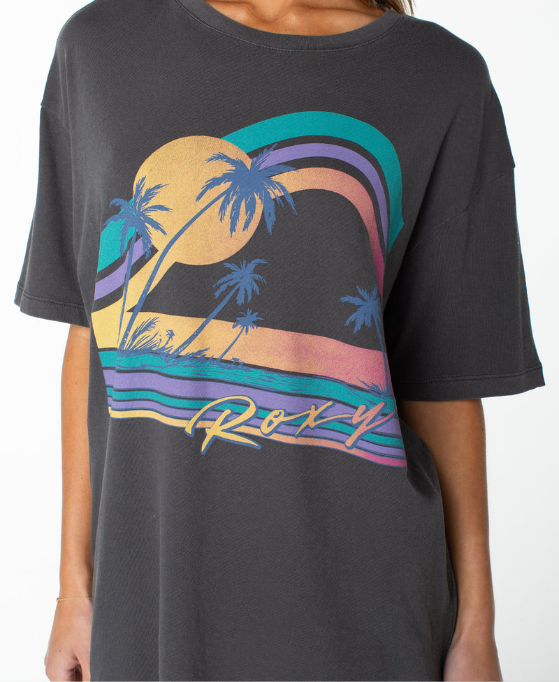 Wearing the Roxy Heatwave Oversized Tee, featuring a bold graphic of a colorful vintage sunset with palm trees and stripes on the front, along with “Roxy” in cursive. This black tee offers an effortlessly stylish and comfortable look with its relaxed drop shoulder fit.
