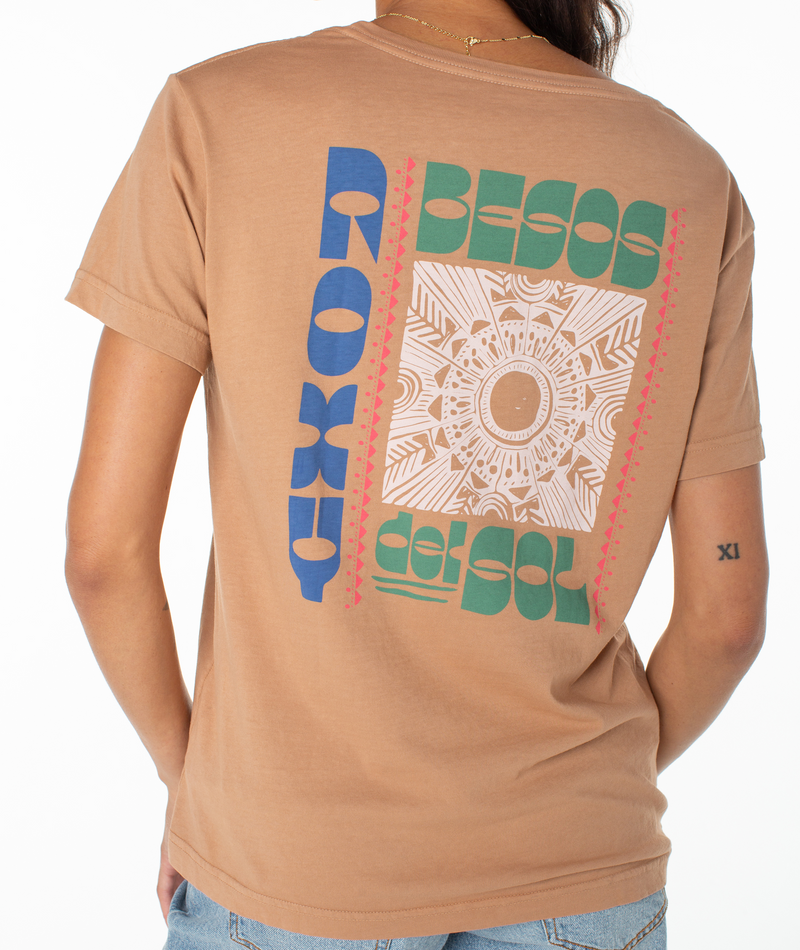 A person wearing a tan Besos Tee with a graphic on the back featuring the text Roxy Besos del sol and a central geometric sun design.
