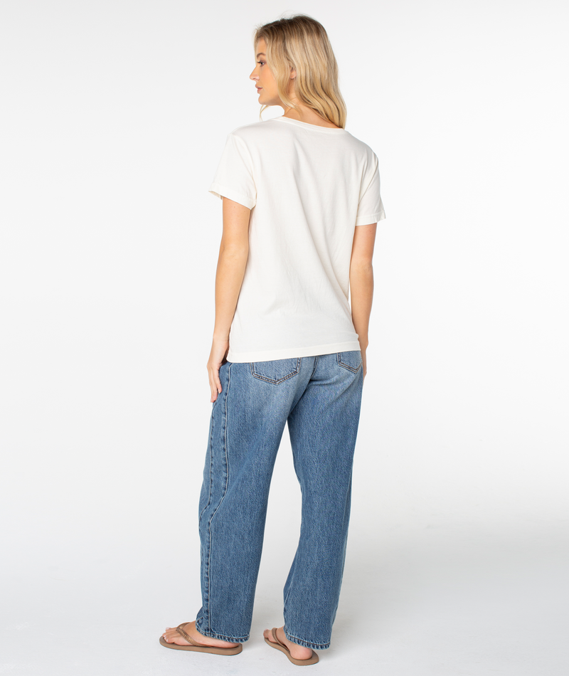 A person seen from behind wearing a white Dad Vibes Surfboard Tee and blue jeans.