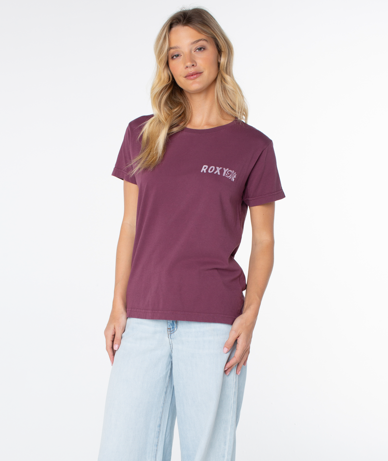 A person wears a slouchy, short-sleeve, dark red Roxy Simple Palm Top with a white logo printed on the left chest and light wash jeans.