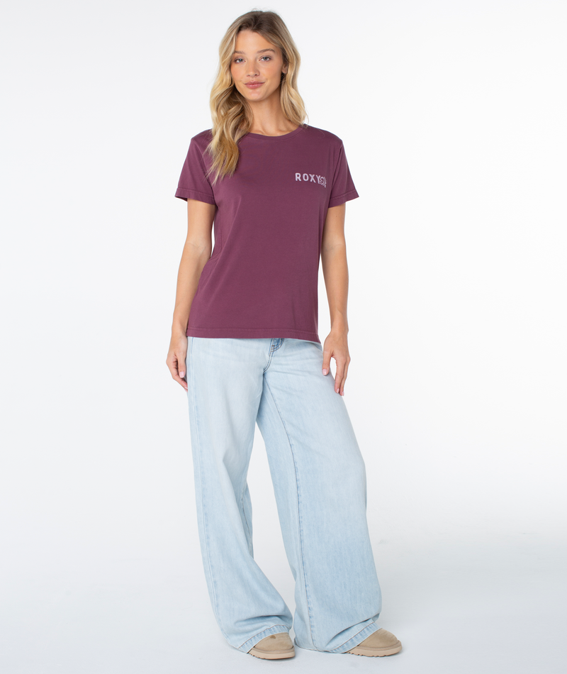 A woman wearing a maroon Roxy Simple Palm top with a small white logo on the chest and light-wash wide-leg jeans.