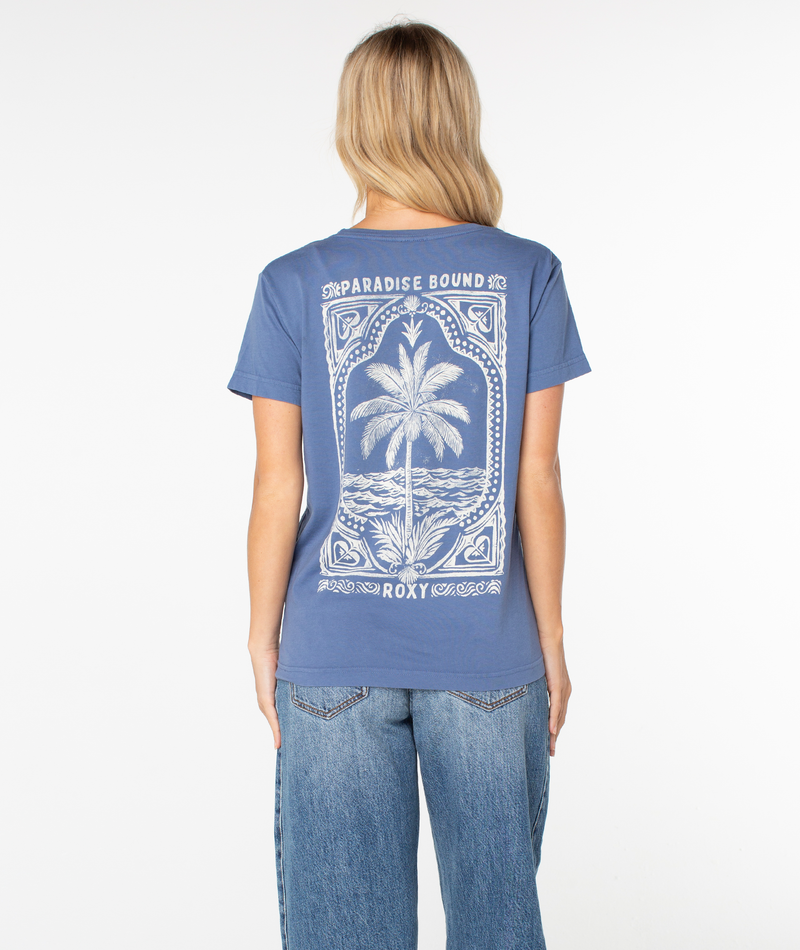 A person wears a slouchy, beachy Roxy Simple Palm Top featuring a blue t-shirt back graphic with a palm tree inside an ornate frame, the text PARADISE BOUND at the top, and ROXY at the bottom.