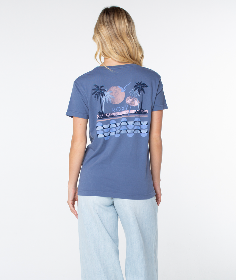 A person seen from behind wearing a blue Roxy Palm Geo Top featuring a back graphic of a sunset, palm trees, an umbrella, and stylized waves.