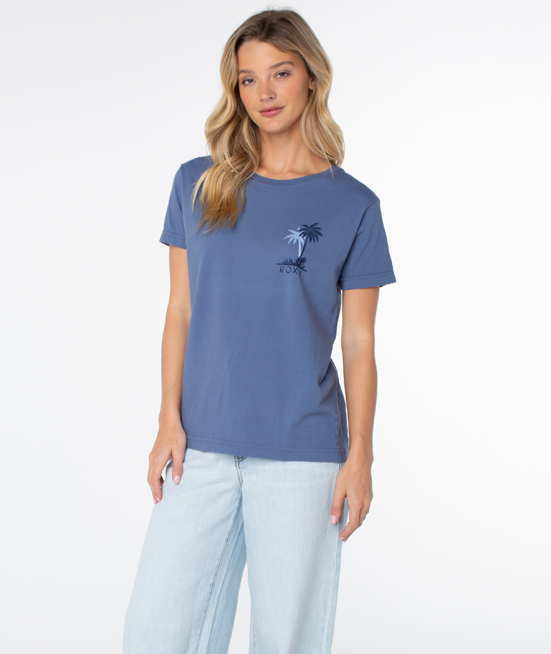A woman wears a blue slouchy Roxy Palm Geo Top with a small palm tree graphic and logo on the chest, paired with light-wash jeans.