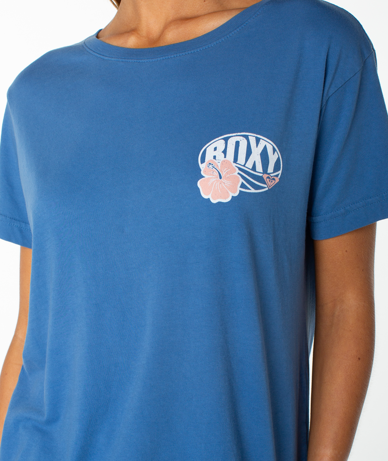 A person wearing the OG Roxy Oval Boyfriend Crew by Roxy, a blue slouchy top featuring a small graphic with the word “ROXY” and a pink hibiscus flower on the left chest.