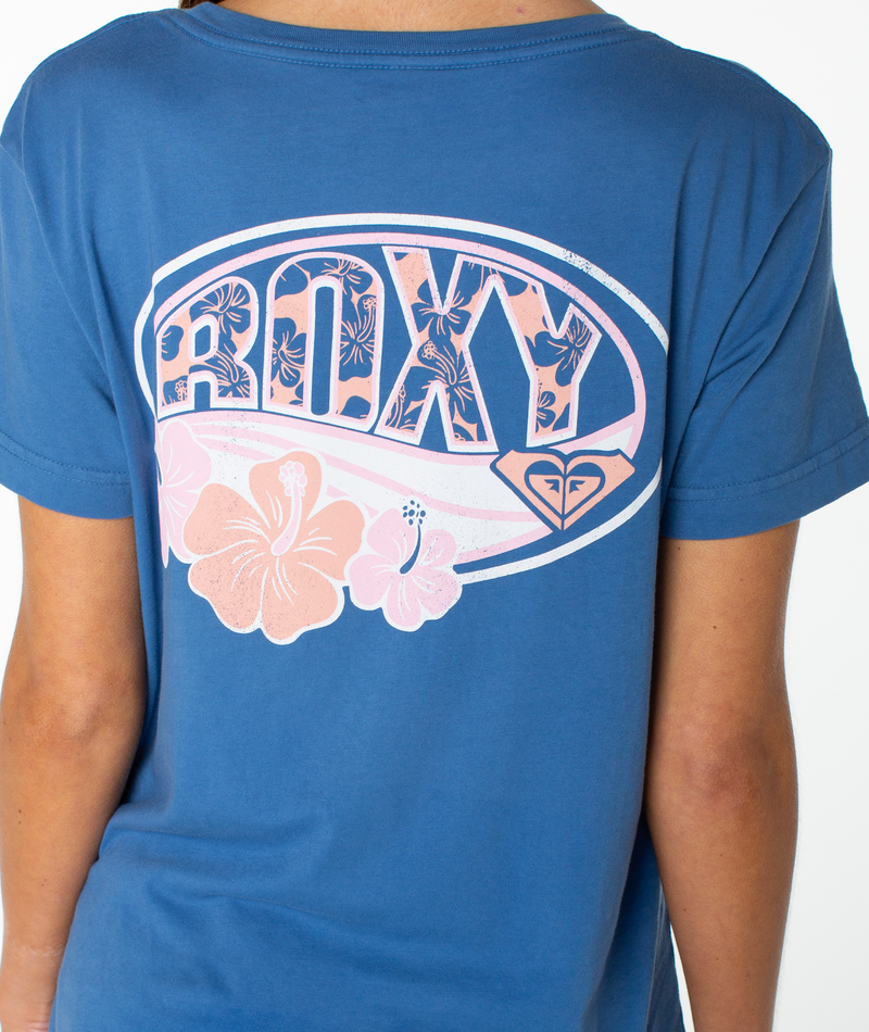 A person wearing the OG Roxy Oval Boyfriend Crew by Roxy—a blue slouchy top featuring large “ROXY” lettering, floral patterns with pink hibiscus flowers, and the Roxy logo on the back.