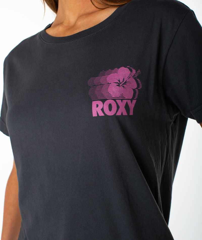 A person wearing the Roxy Surf Team Boyfriend Crew, a dark slouchy top featuring a pink hibiscus flower graphic and “ROXY” printed on the chest.