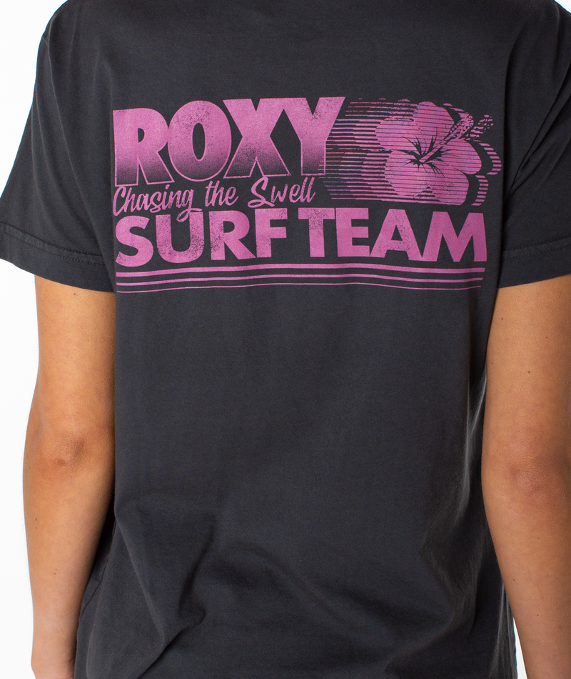 A person is wearing the Roxy Surf Team Boyfriend Crew, a dark slouchy top with pink text and a flower graphic on the back that reads “ROXY Chasing the Swell SURF TEAM.” Only the back of the shirt and part of one arm are visible.