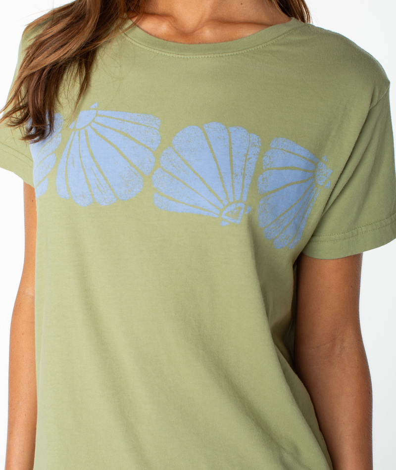 A person wearing the Shell Band Boyfriend Crew by Roxy, featuring a light green color and three blue seashell designs across the chest.