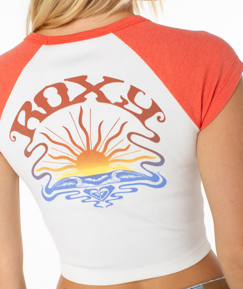 A person wearing the Roxy Garrett Wave Tee, a white and red spring crop top featuring a sunrise over waves graphic and "ROXY" printed on the back.