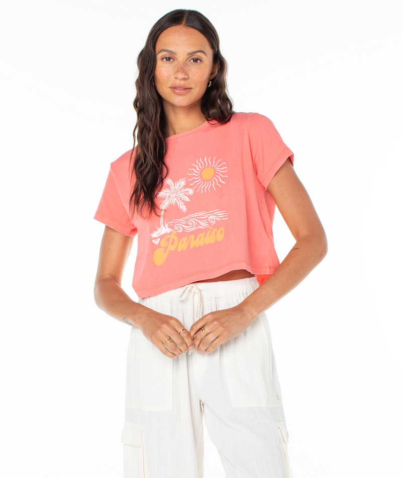 A woman wearing a white drawstring pant outfit and a pink Roxy Paraiso Screen Tee featuring a palm tree, sun, waves, and the word Paraiso.