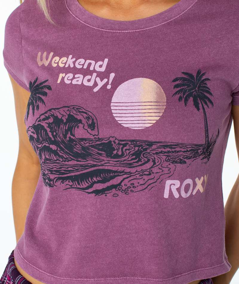 A Tulipwood Weekend Ready Top featuring a coastal cool graphic of a sunset, ocean wave, and palm trees, with the text Weekend ready! printed above this purple cap-sleeve staple.