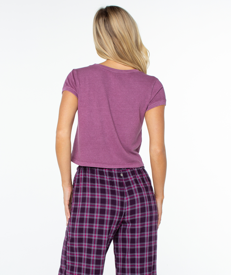 A person seen from behind wears a breezy, short-sleeved mauve Weekend Ready Top by Roxy with purple plaid pajama pants.