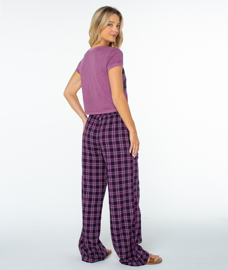 A person wears a Weekend Ready Top in dark purple with short sleeves and loose-fitting, purple and black plaid trousers.