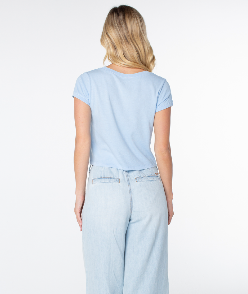 Back view of a person wearing a light blue, breezy fit Roxy Adventures Tee and light-wash denim pants, a versatile spring staple.