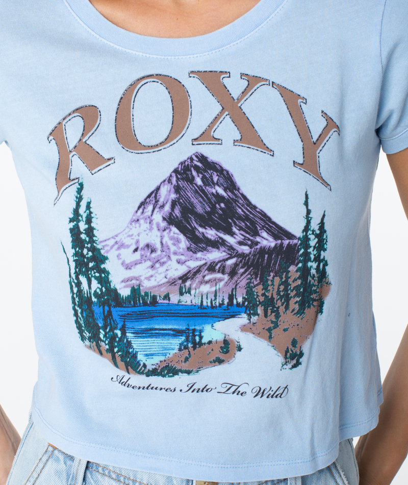 Light blue short-sleeved Roxy Adventures Tee featuring a mountain and lake graphic with the text ROXY above and Adventures Into The Wild below, a breezy fit for a coastal cool graphic essential.