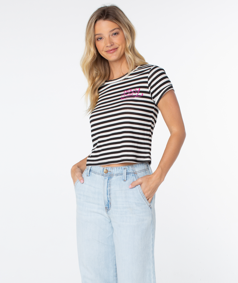 A woman with long blonde hair wears the Roxy Vintage Roxy Stripe Top featuring black-and-white stripes and merci in pink, paired with light blue jeans—spring-ready style, hands in pockets against a white background.