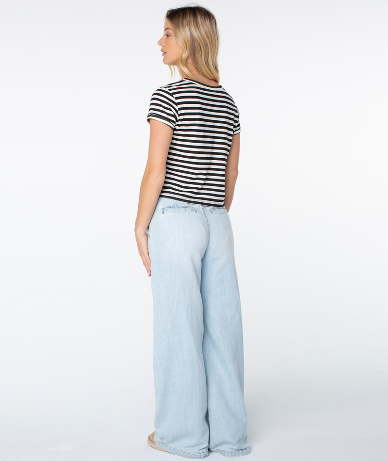 A woman faces away, wearing the Vintage Roxy Stripe Top by Roxy—a black and white striped short-sleeve top—paired with light blue wide-leg jeans, set against a plain white background.