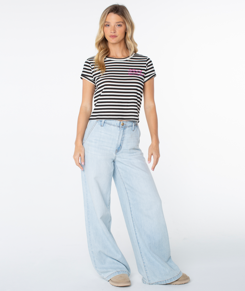 A woman in the Vintage Roxy Stripe Top by Roxy in Phantom Vintage Roxy, paired with light blue wide-leg jeans and beige shoes, stands facing forward against a white background, highlighting this spring-ready style.