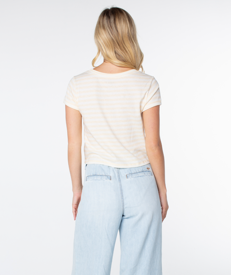 A woman with long blonde hair models the Vintage Roxy Stripe Top by Roxy with light blue jeans, standing facing away from the camera against a plain white background.