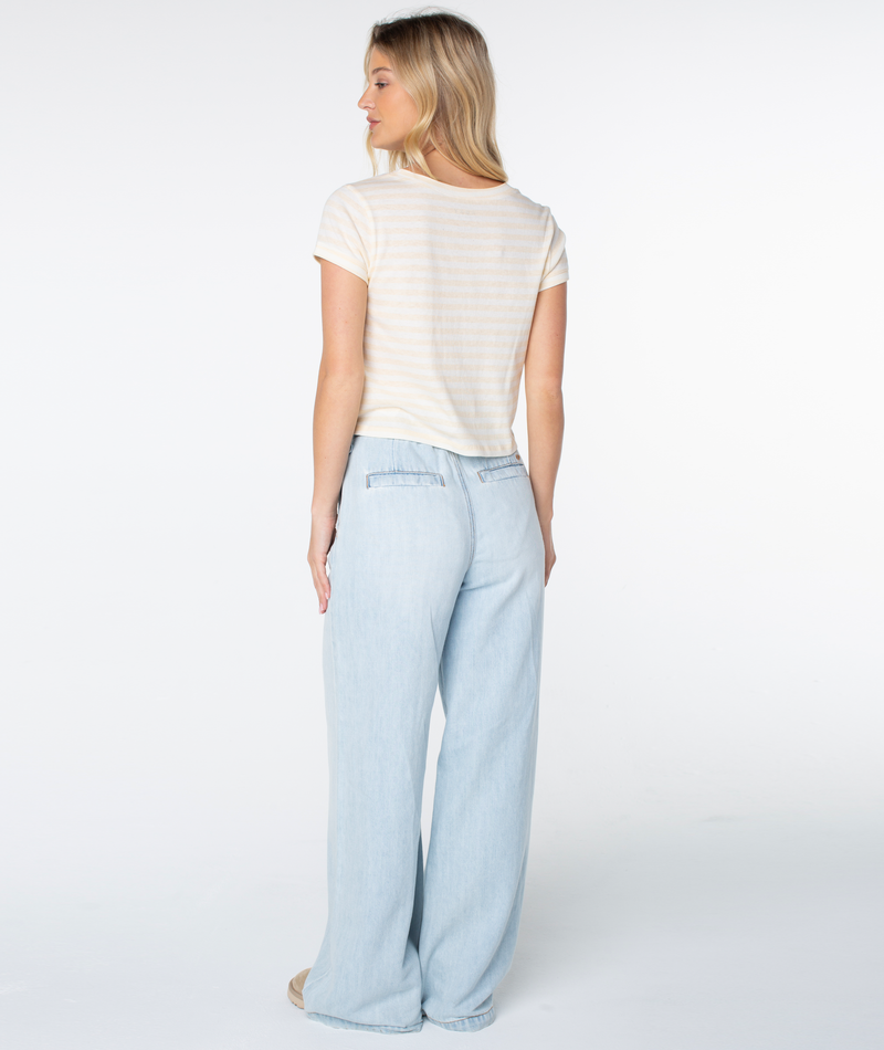 A woman faces away in the Vintage Roxy Stripe Top by Roxy and high-waisted, wide-leg light blue jeans. Her long blonde hair flows in a studio with a plain white background—a spring staple.