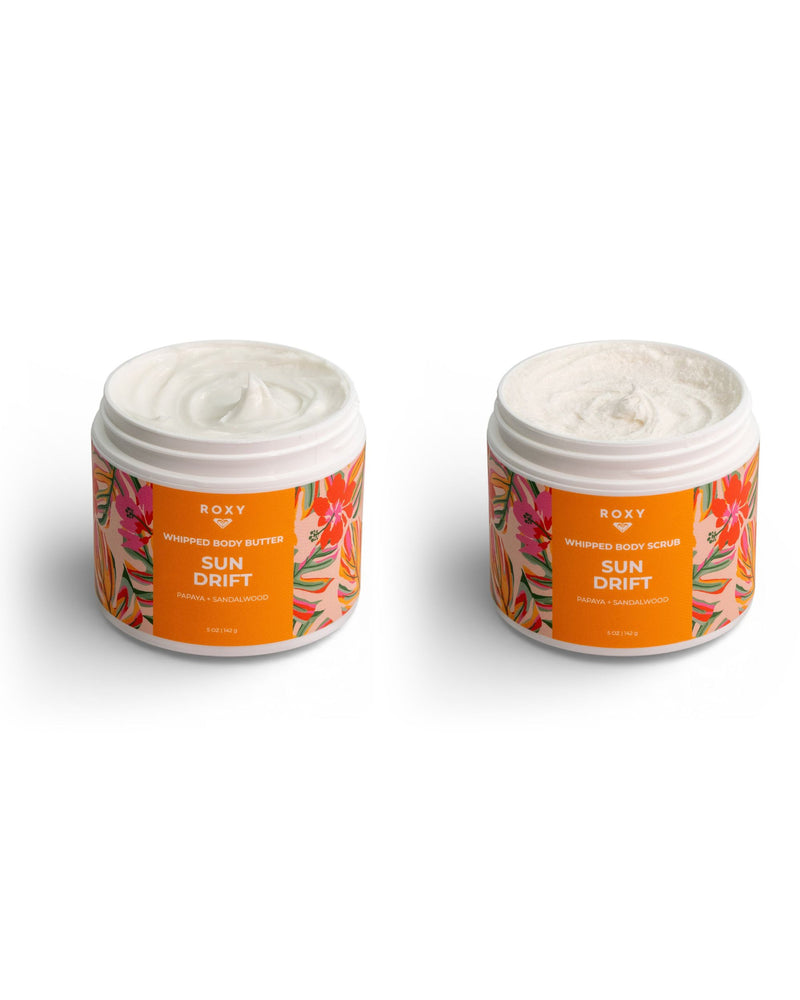 Two open jars from the ROXY Sun Drift Body Butter & Scrub Bundle, distinguished by vibrant orange floral labels and white lids placed beneath them, promise silky-soft skin. The left jar contains the whipped body butter, while the right features an exfoliate and hydrate whipped body scrub—both infused with lush tropical notes. Each displays creamy, textured contents designed for a luxurious skincare experience.