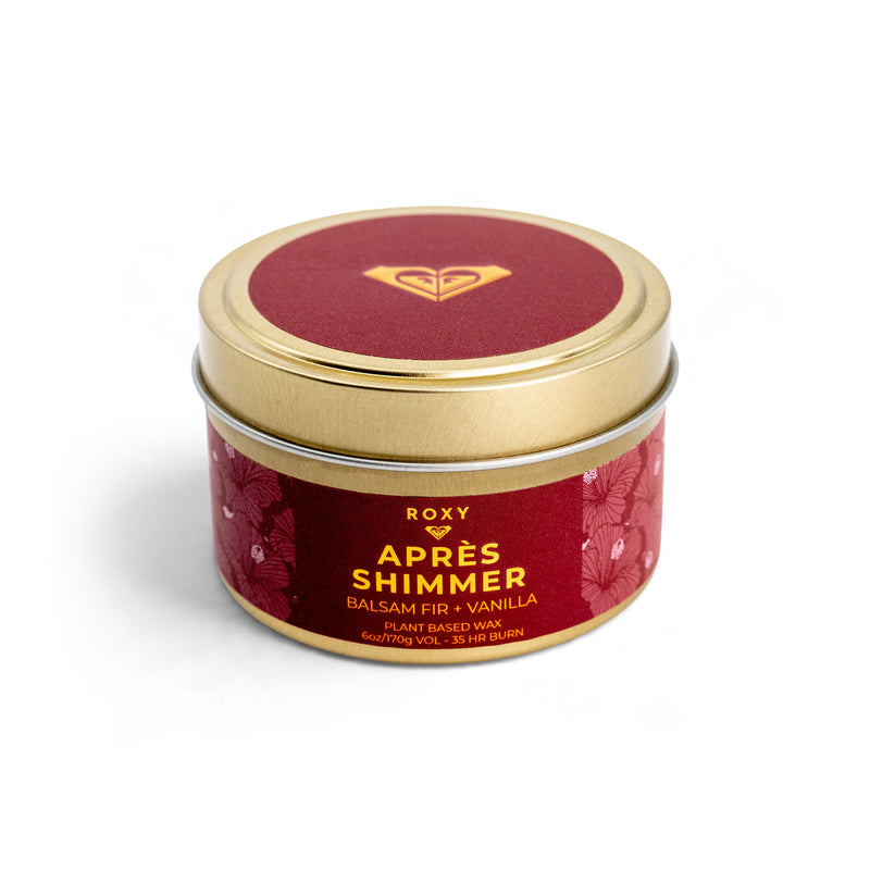 ROXY Apres Shimmer Holiday Tin Candle in a red tin with a gold lid, featuring notes of balsam fir and vanilla for winter luxury.