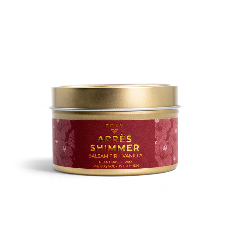 A gold-lidded ROXY Apres Shimmer Holiday Tin Candle with a red floral label, featuring the scent of balsam fir and vanilla, perfect for winter luxury.