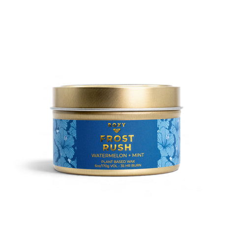 ROXY Frost Rush Holiday Tin Candle in a gold metal tin with a blue floral label featuring crisp mint and watermelon scents.