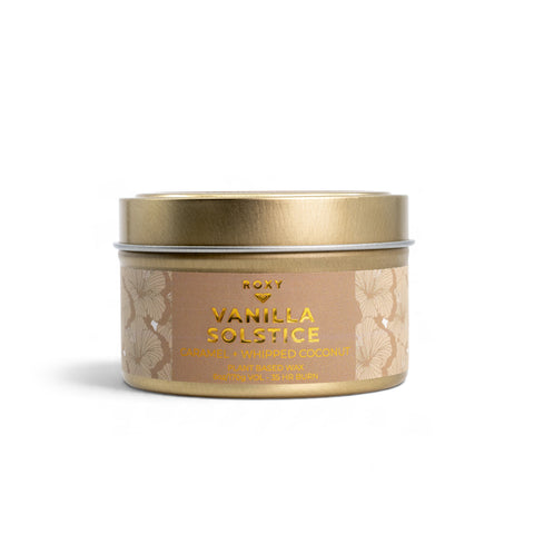 A gold-toned metal Vanilla Solstice Holiday Tin Candle with a label featuring notes of caramel and whipped coconut.