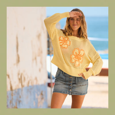Woman wearing a yellow sweater with floral designs on a beach.