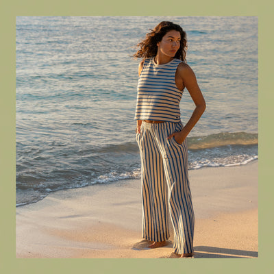 Woman in a striped outfit standing on a beach with ocean waves in the background