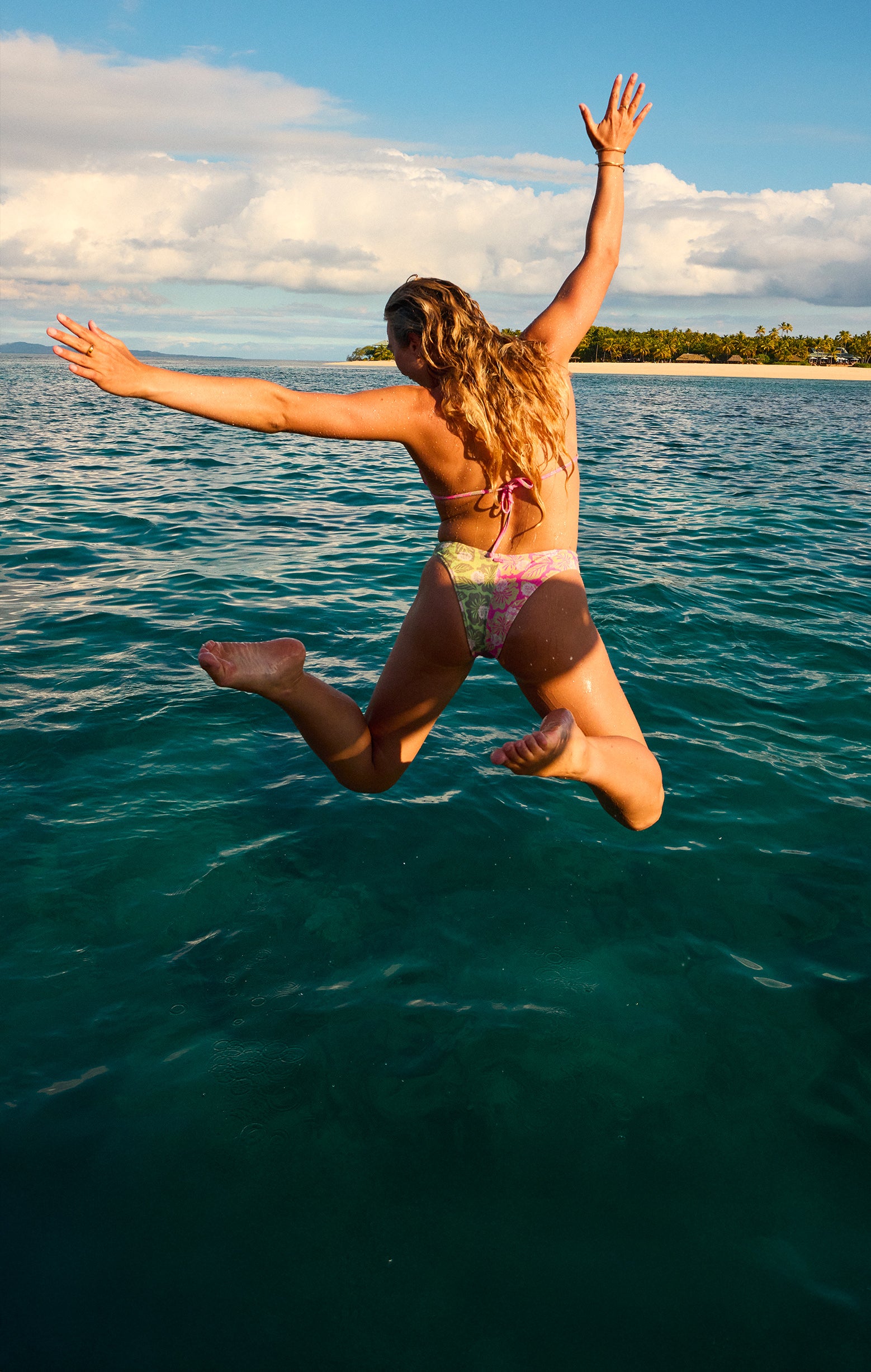 Person jumping into the ocean with arms outstretched, surrounded by clear blue water and a bright blue sky.