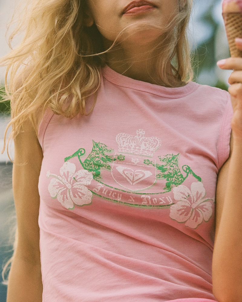 A woman outdoors holds an ice cream cone while wearing the Roxy x Juicy Crest Tank Top by Roxy, a candy pink cotton tank featuring a crown, hibiscus flowers, and a logo crest in white and green.