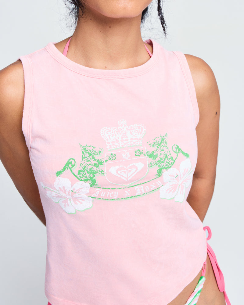 A woman models the Roxy x Juicy Crest Tank Top in candy pink, featuring a green and white floral crest, with matching bikini bottoms. She's set against a plain light background, her face partly out of frame.